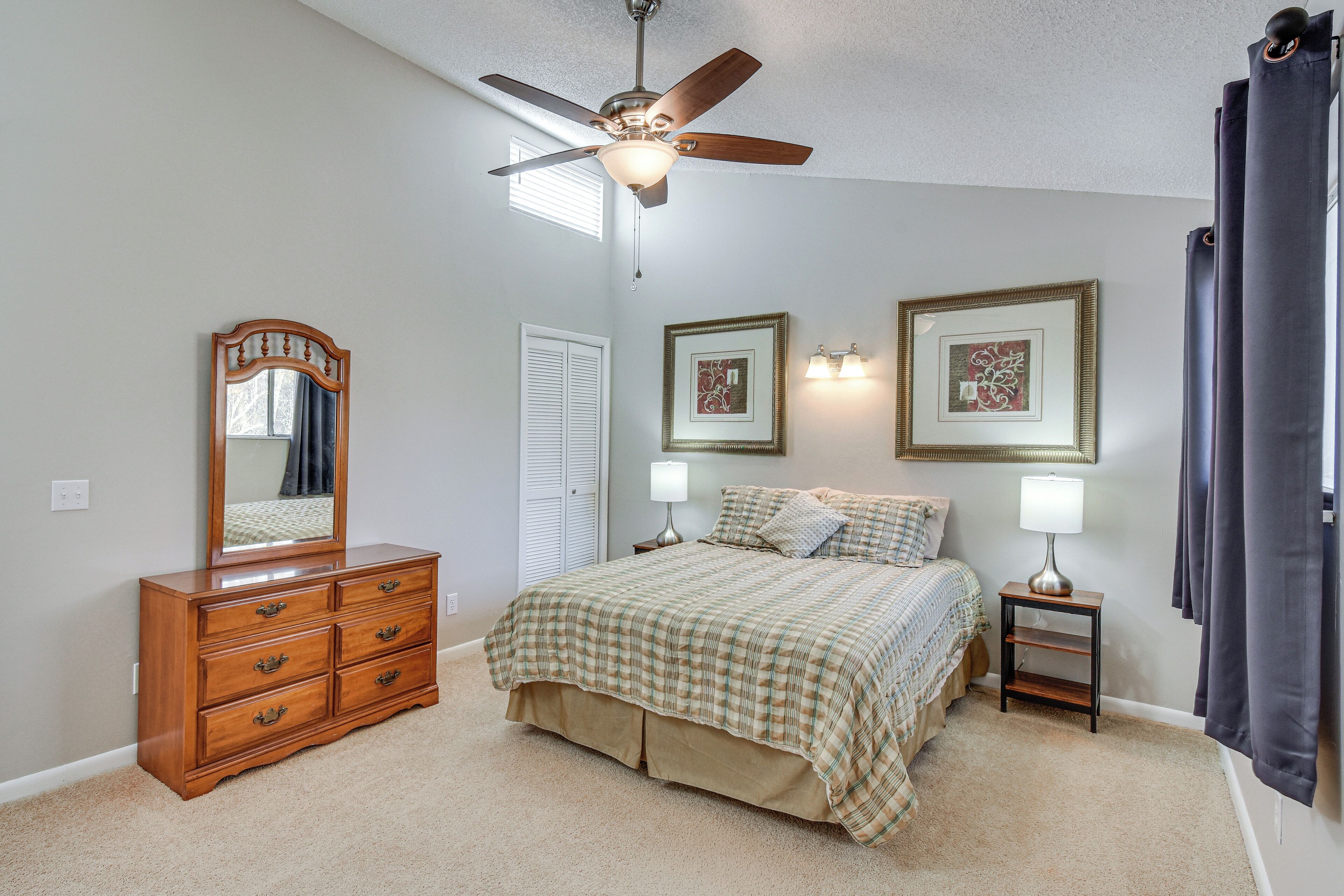 A bedroom with a bed, dresser, ceiling fan, bedside lamps, and framed artwork.