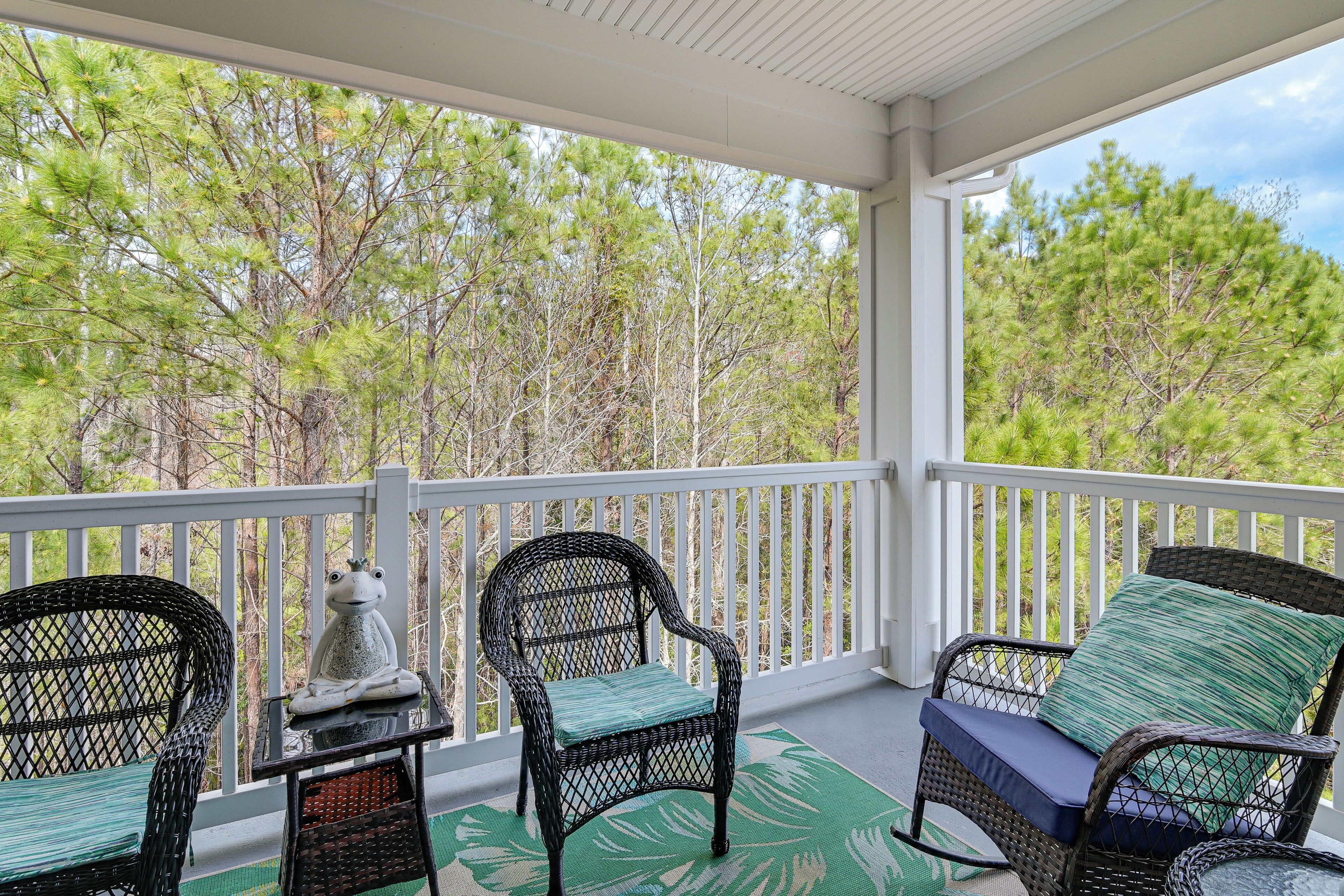 A covered porch with wicker chairs and a table, overlooking a forested area.