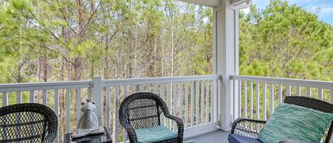 A covered porch with wicker chairs and a table, overlooking a forested area.