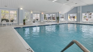 En inomhuspool med klart vatten, omgiven av vita stolar och krukväxter.