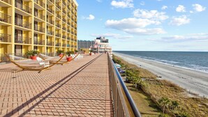 Ett hotell med utsikt över stranden, en asfalterad gångväg och utomhusmöbler.