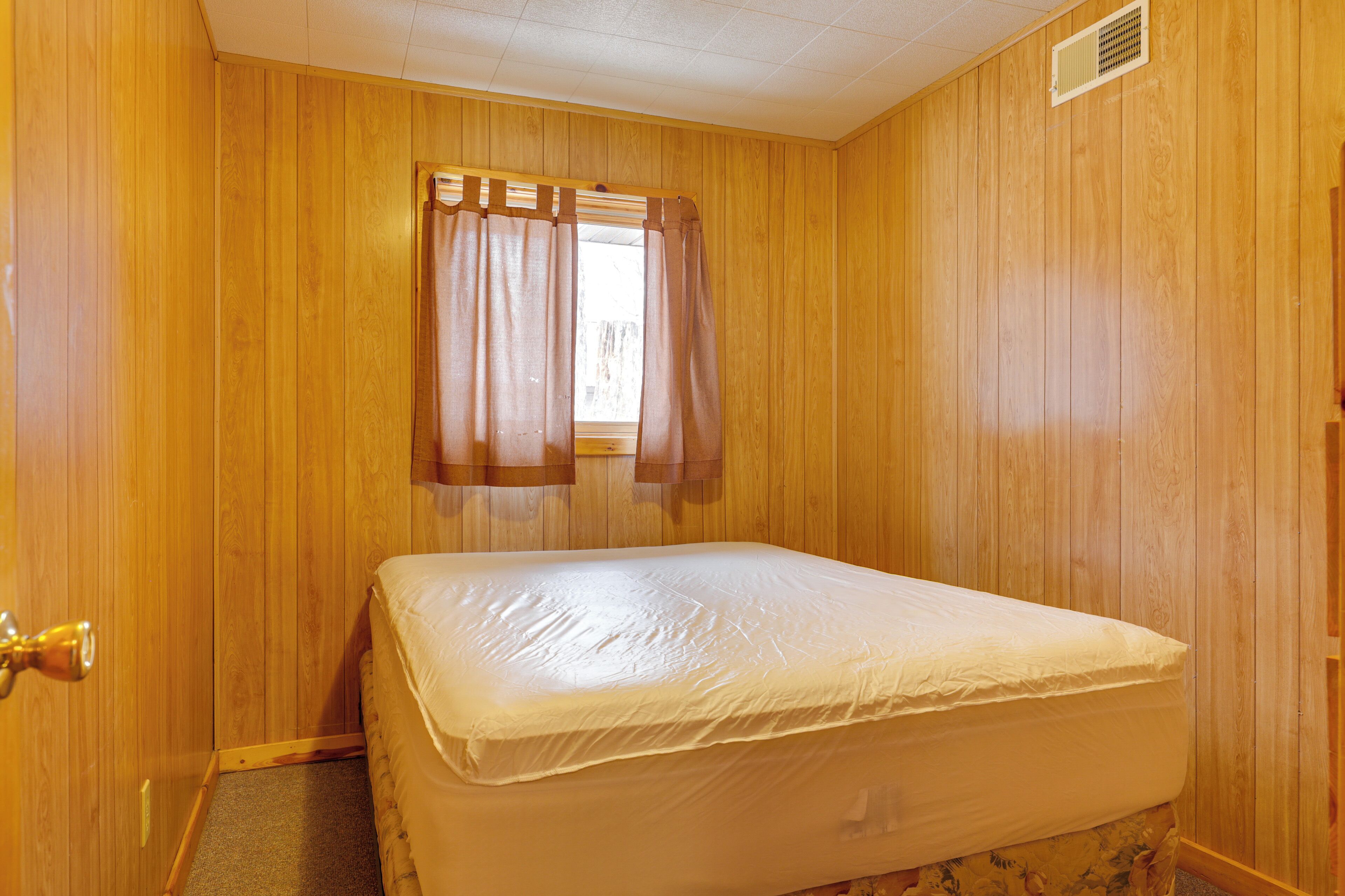 Una stanza con rivestimenti in legno, un letto con materasso, una finestra con tende e una porta con maniglia.