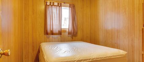 Una stanza con rivestimenti in legno, un letto con materasso, una finestra con tende e una porta con maniglia.
