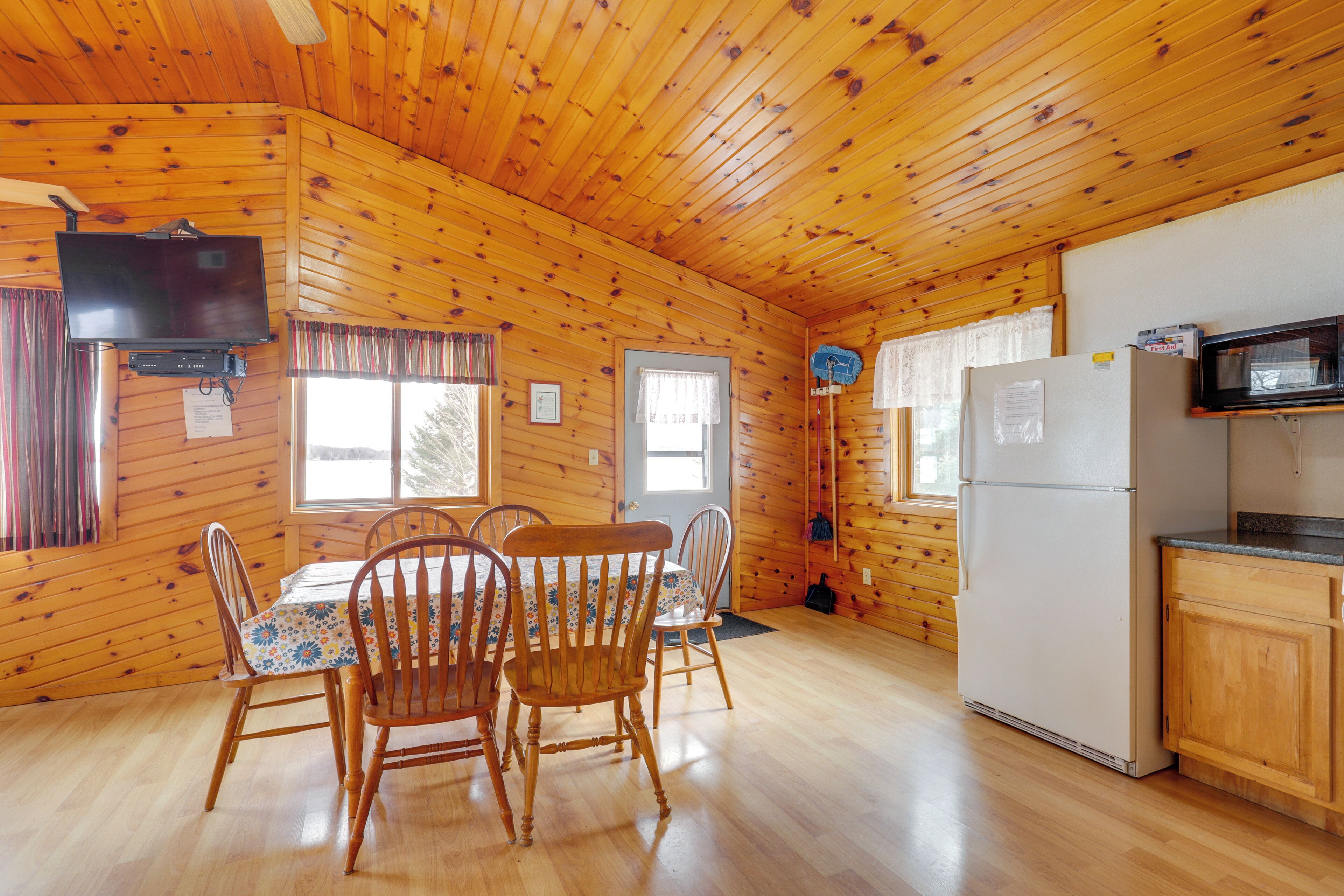 Interno di una baita in legno con un tavolo da pranzo, sedie, televisore, frigorifero e microonde.