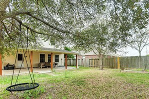 A backyard with a swing, a covered patio, and a wooden fence.