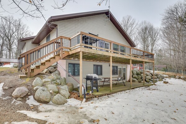 A two-story house with a wooden deck, a covered patio, and a stone wall. - Fishing Paradise: Lakefront Duplex in Northwoods (Pearson)