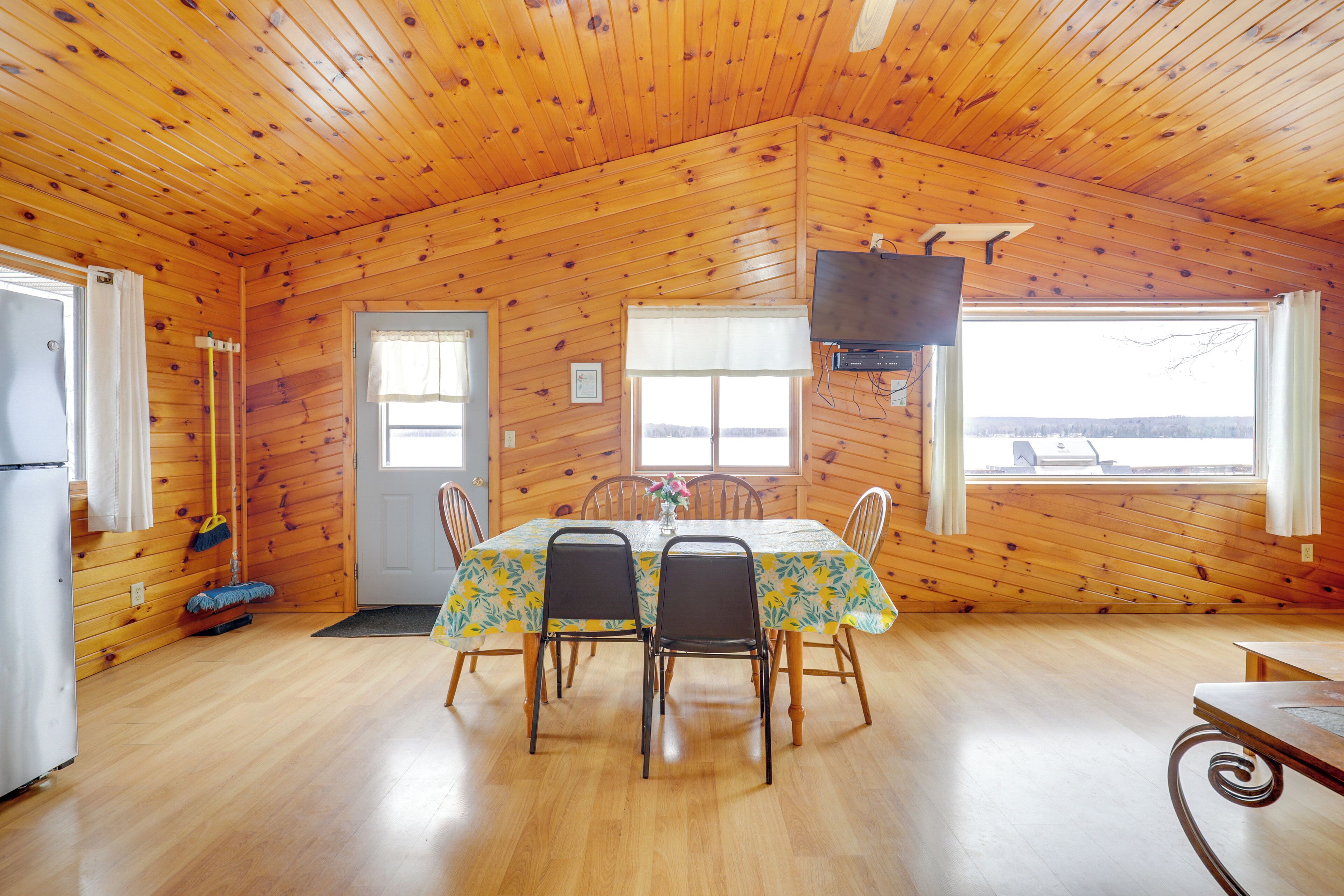 A wooden cabin with a dining table, chairs, a television, and a view of the outside.