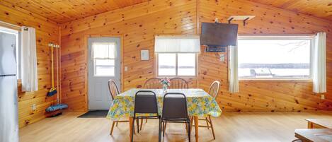 A wooden cabin with a dining table, chairs, a television, and a view of the outside.