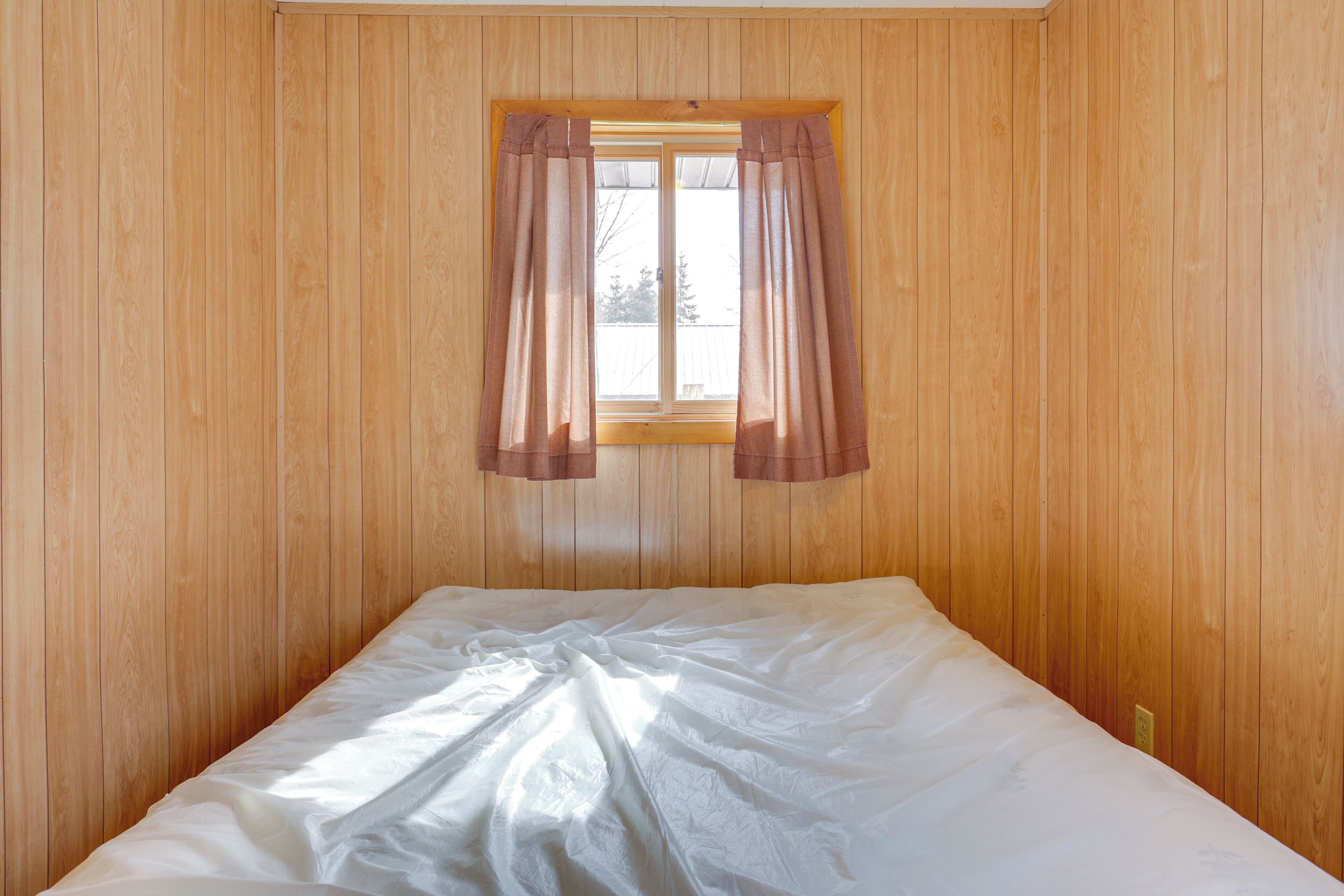 Una cama individual en una habitación con paredes de madera y una ventana con cortinas.