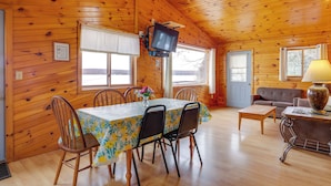 L'intérieur d'un chalet en bois comprend une table à manger, des chaises, un canapé, un téléviseur fixé au mur et une fenêtre.