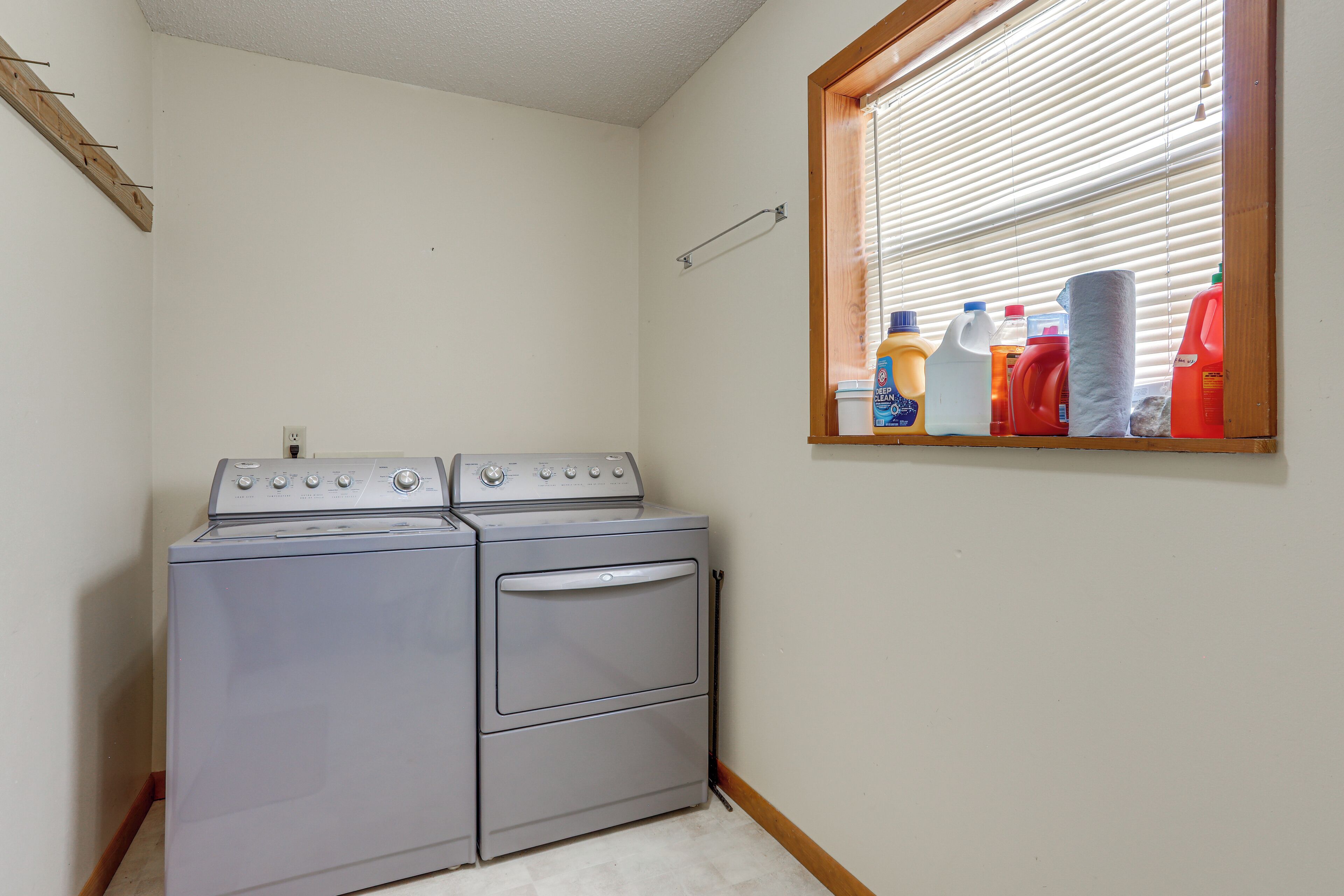 A laundry area with a washer and dryer, a window with blinds, and laundry supplies on the windowsill.