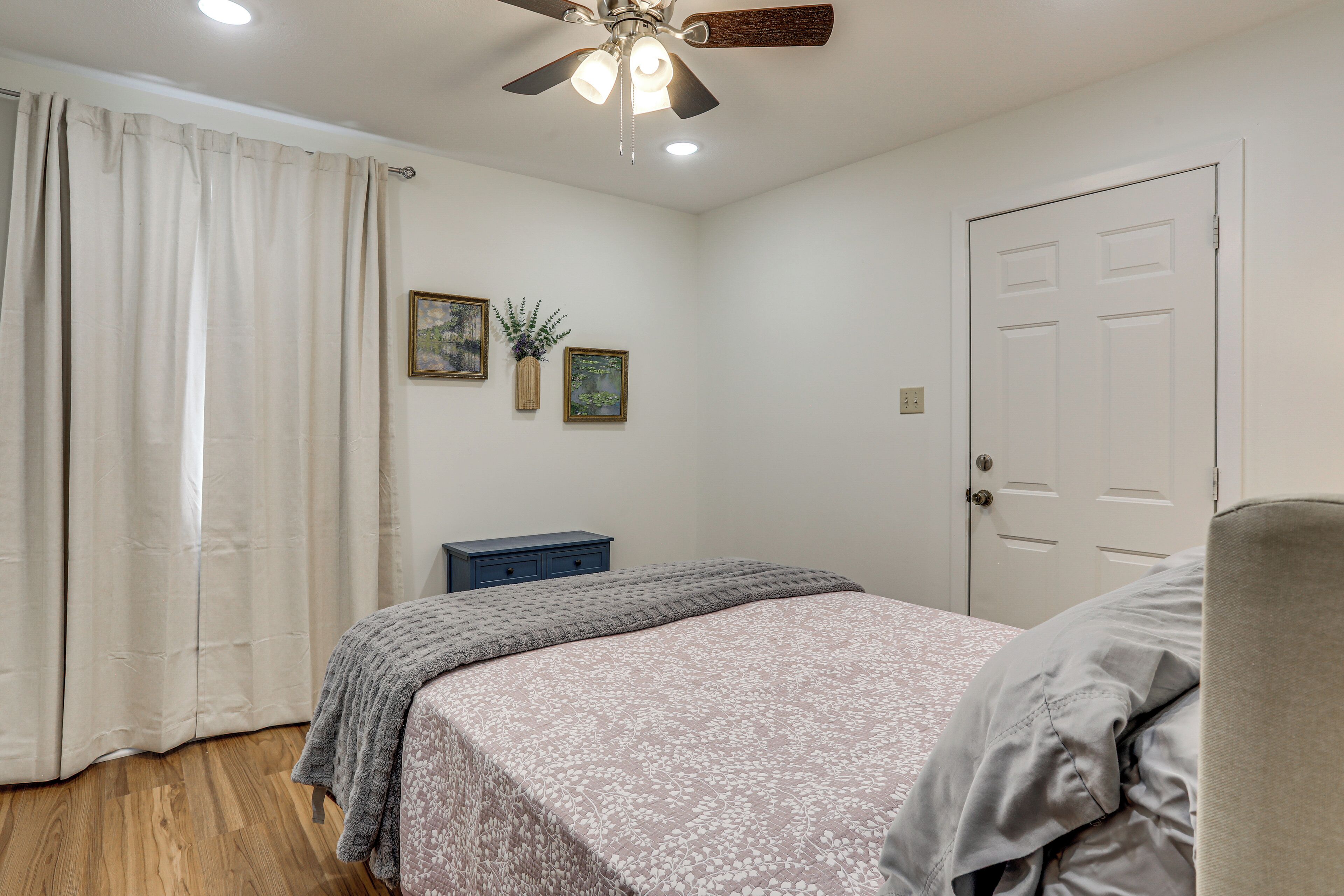 A bedroom with a bed, a ceiling fan, a door, and a nightstand.