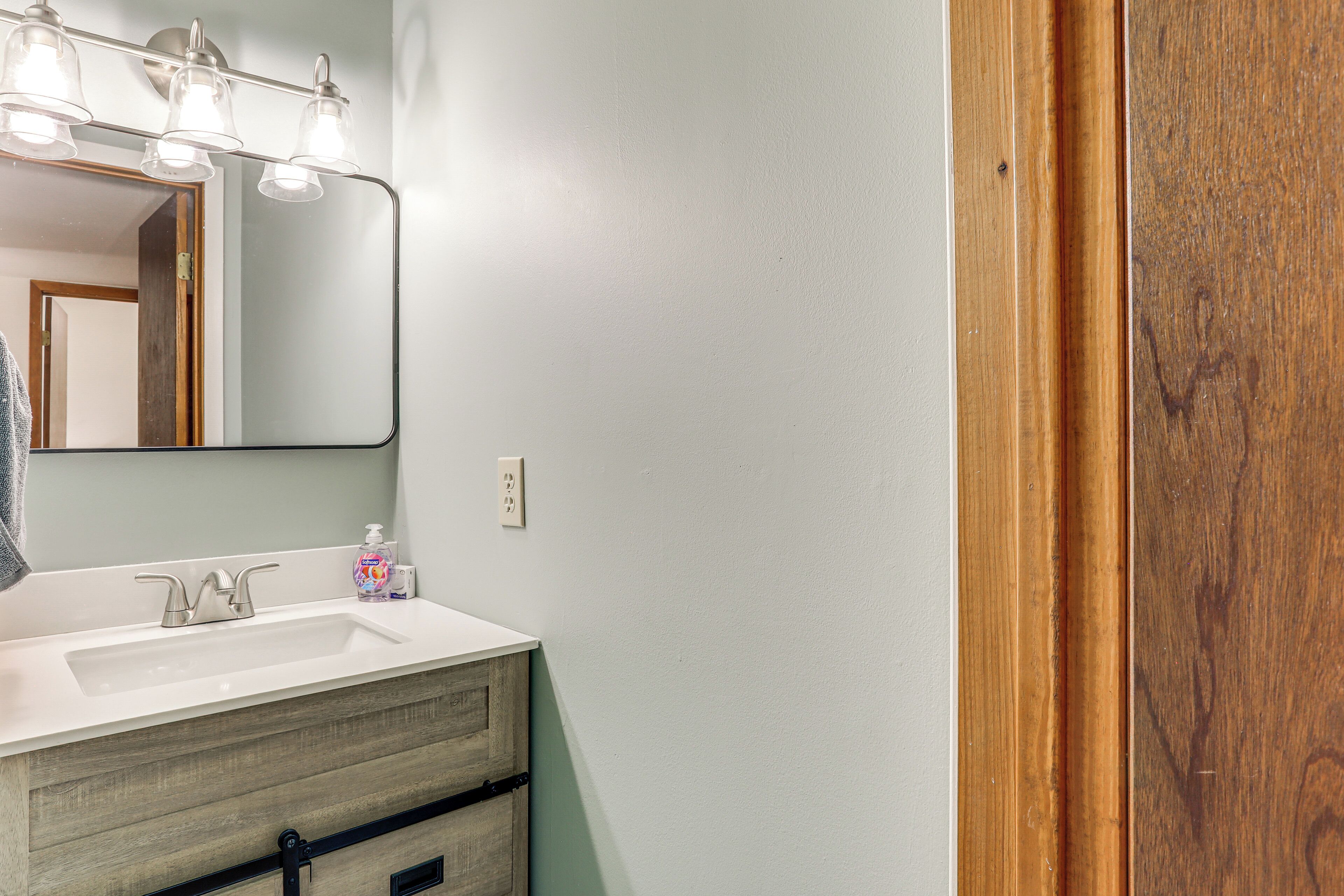 Un baño con lavamanos blanco, tocador de madera y un espejo con tres luces.
