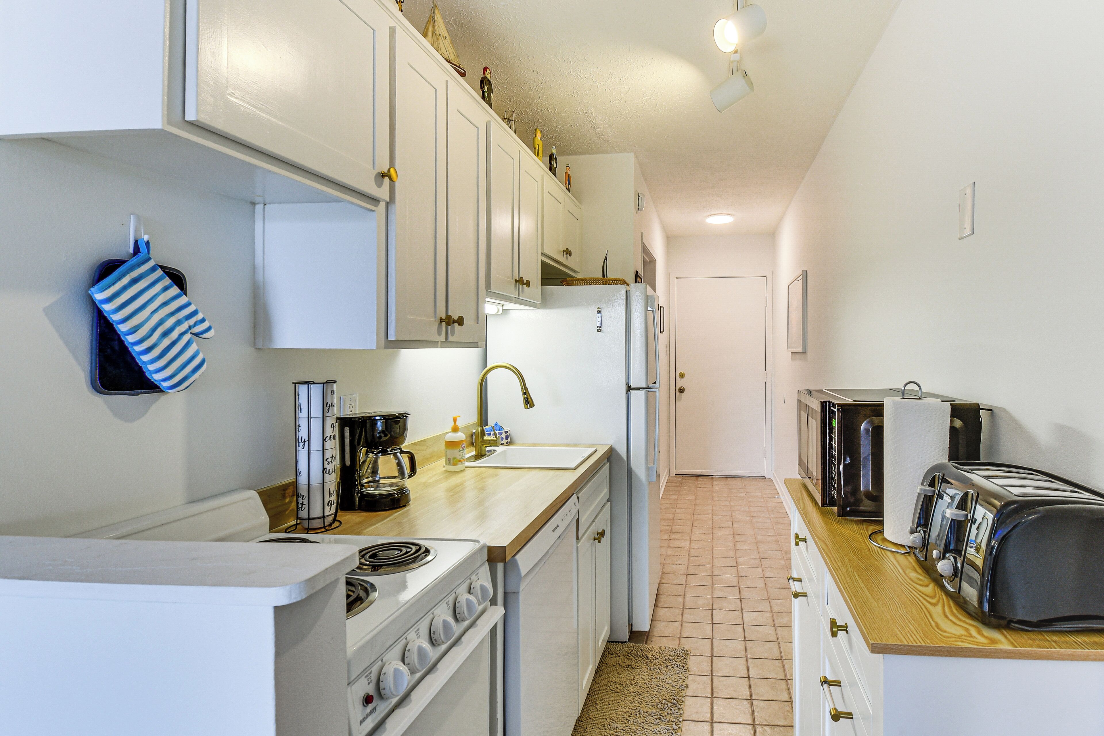 Une cuisine de taille réduite avec des meubles blancs, une cuisinière, un évier et un grille-pain.