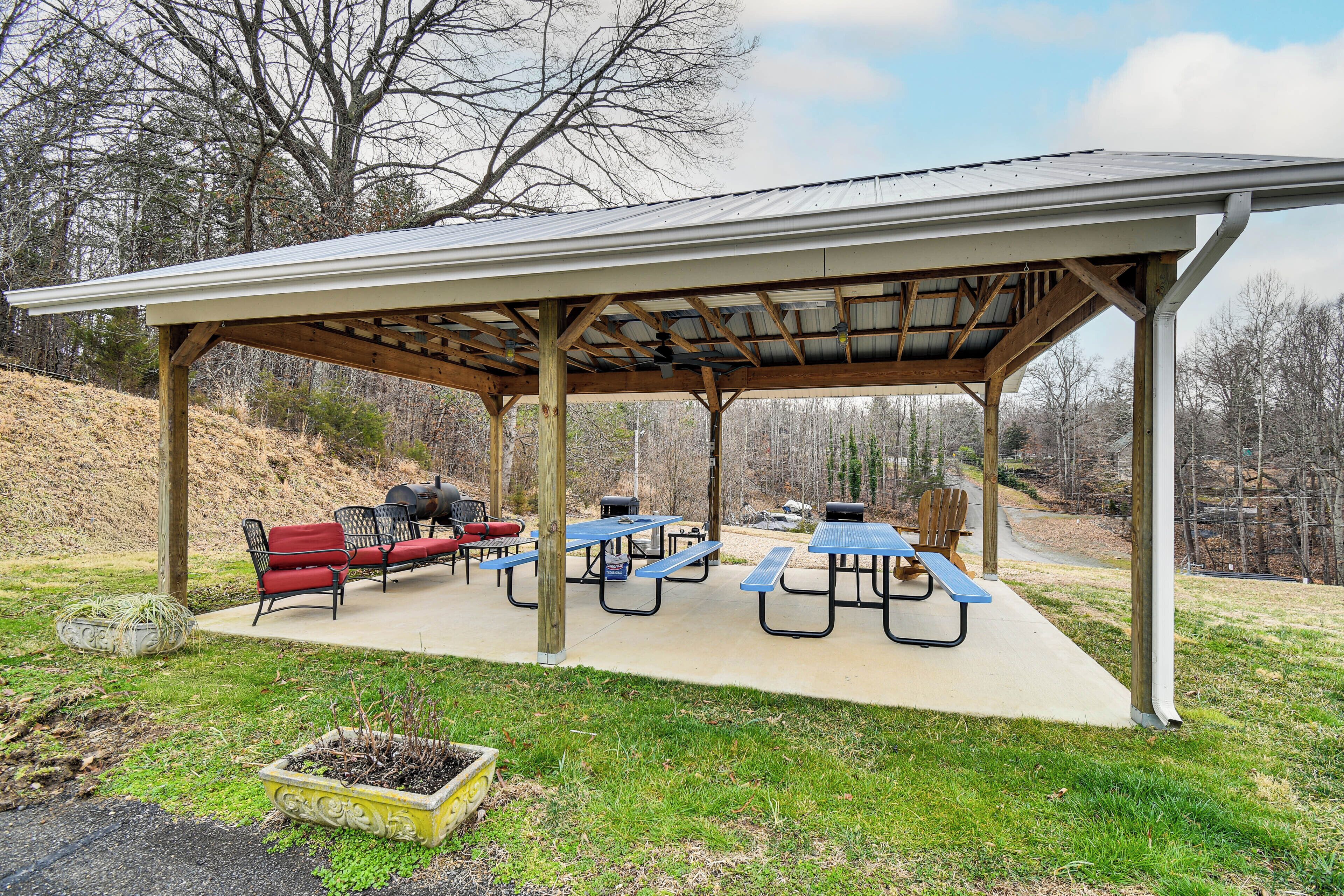 A covered picnic area with benches and tables, surrounded by trees.