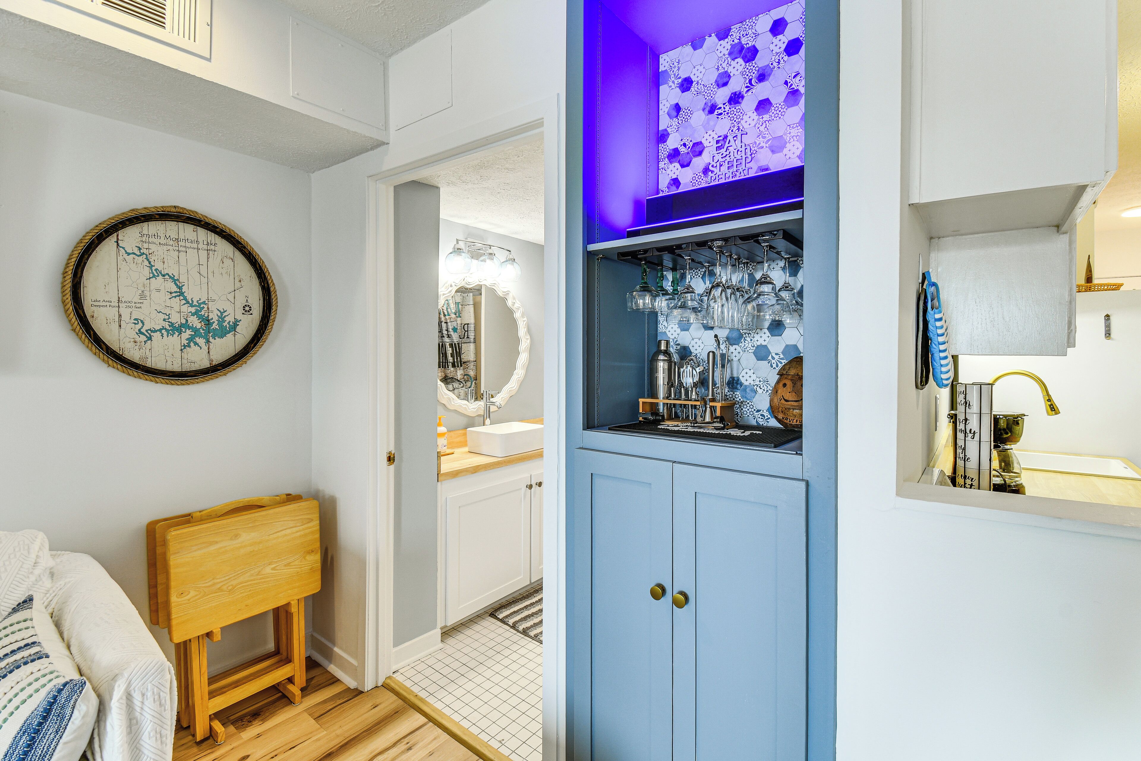 A bathroom with a wooden bench, a map, a mirror, and a shelf with glassware.