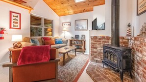 A cozy living room with a wooden ceiling, a brick fireplace, and a large window. - Rustic Mtn-view Home w/ Wood Stove: Dog Friendly (Felton)