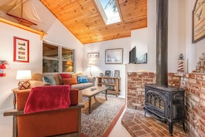 A cozy living room with a wooden ceiling, a brick fireplace, and a large window. - Rustic Mtn-view Home w/ Wood Stove: Dog Friendly (Felton)