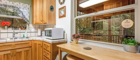 Een keuken met houten kastjes, een magnetron, een spoelbak en een raam met uitzicht op een balkon.