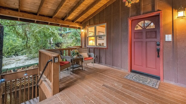 A wooden deck with a red door, wicker chairs, and a glass door leading to a room. - Rustic Mtn-view Home w/ Wood Stove: Dog Friendly (Felton)