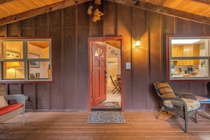 A wooden interior with a red door, wicker furniture, and a visible kitchen area. - Rustic Mtn-view Home w/ Wood Stove: Dog Friendly (Felton)