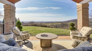 Une terrasse couverte avec une table ronde et deux chaises, un mur en briques et une vue sur un champ verdoyant.