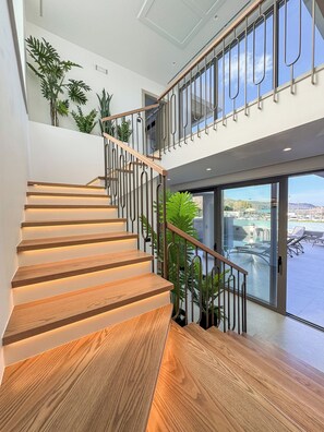 Un escalier moderne avec des marches en bois et des rampes en métal, menant à un balcon doté de portes vitrées et de plantes en pot.