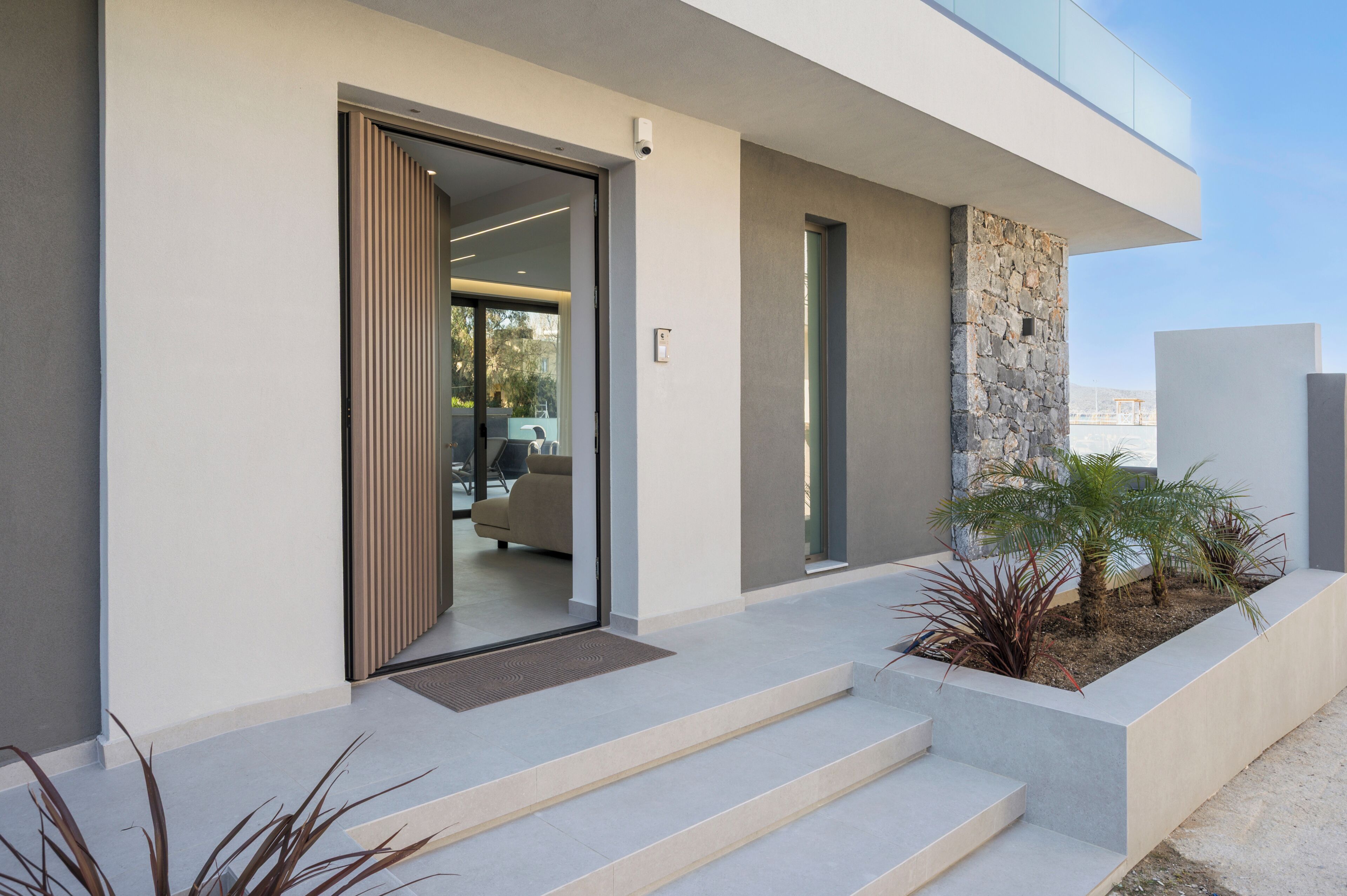 A modern building with a glass door entrance, a stone accent wall, and a small outdoor planter with plants.