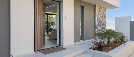 A modern building with a glass door entrance, a stone accent wall, and a small outdoor planter with plants.