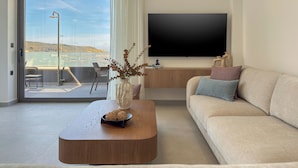 Un salon moderne comprenant un canapé, une table basse agrémentée d’objets décoratifs, un téléviseur à écran plat et une vue sur un balcon aménagé avec du mobilier d’extérieur.