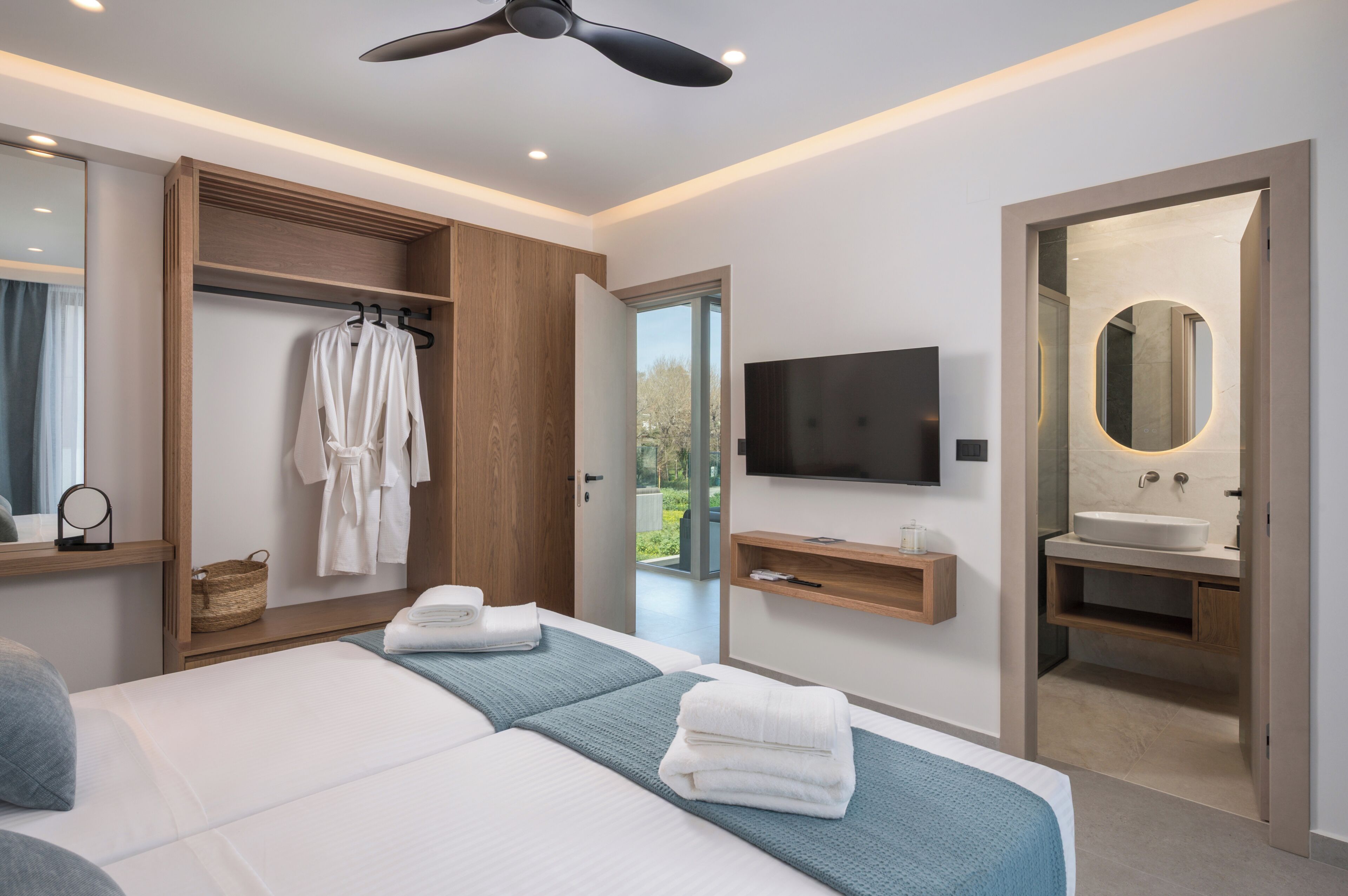 A modern hotel room with a bed, a TV, a wardrobe, and a bathroom with a mirror and sink.