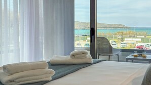 Une chambre d’hôtel avec un lit, une fenêtre avec des rideaux légers, une vue sur un parking et une table avec deux verres.