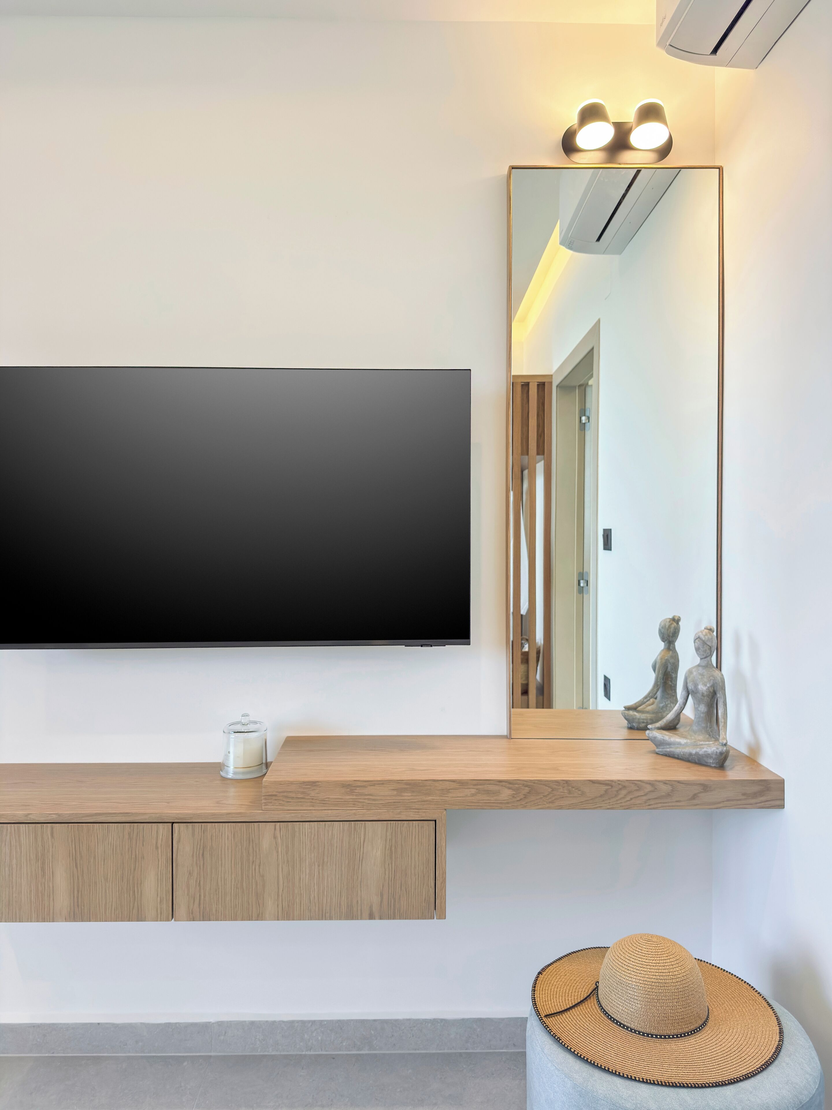 Quarto moderno com televisão na parede, um console de madeira, um espelho e uma estátua decorativa.