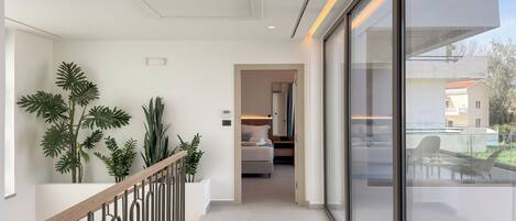 A modern hotel interior with a staircase, potted plants, a bedroom with a bed and nightstand, and a balcony with outdoor furniture.