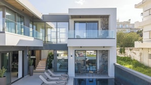 Une maison moderne à deux étages, dotée d’un balcon en verre, d’une piscine et d’un escalier menant à l’étage supérieur.