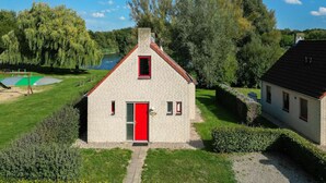 Un petit bâtiment d’un seul étage, avec une porte rouge et une petite fenêtre, entouré de pelouse et d’arbres bien entretenus, et un lac en arrière-plan.
