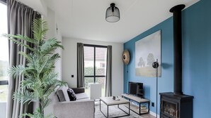 Un salon comprenant un canapé, une table basse, un téléviseur, une cheminée et de grandes fenêtres.
