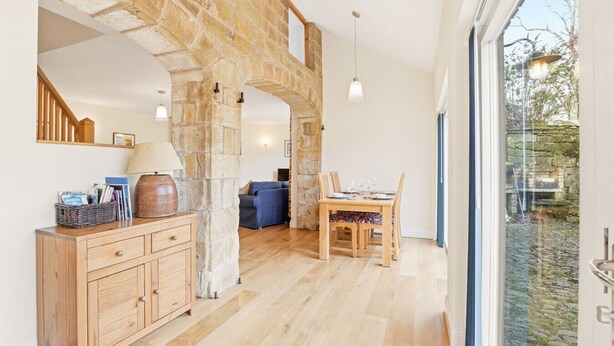 A spacious room with a stone archway, wooden furniture, and a dining area with a view through a large window.