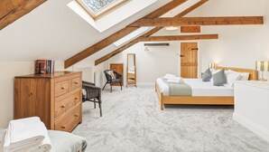 A bedroom with a sloped ceiling, a wooden dresser, a bed with pillows, a chair, and a skylight.