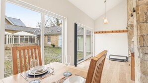 A dining area with a table set for two, a stone wall, and a view of a garden and buildings outside.