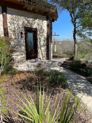 A stone building with a wooden door, a cross, and a pathway leading to it. - The Cross Patio Retreat - Designer Hill Country Studio with Scenic Views (Buda)