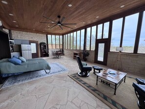 A spacious room with a bed, a chair, a table, and a ceiling fan. - The Cross Patio Retreat (Buda)