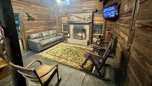 A rustic interior with a fireplace, leather sofa, wooden rocking chairs, and a mounted TV.