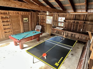 Una mesa de billar, una mesa de ping pong y una silla en una habitación rústica con paredes de madera y techo inclinado.