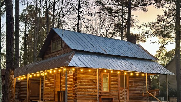 A log cabin with a metal roof, wooden exterior, and a porch with string lights.