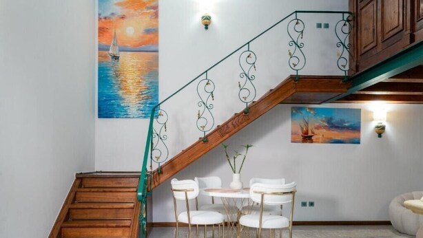 A wooden staircase with a metal railing, a small table with chairs, and two wall-mounted light fixtures. - Apartament 3 (Timișoara)