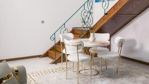 A dining area with a table and chairs, a staircase with a green railing, and a patterned rug. - Apartament 3 (Timișoara)