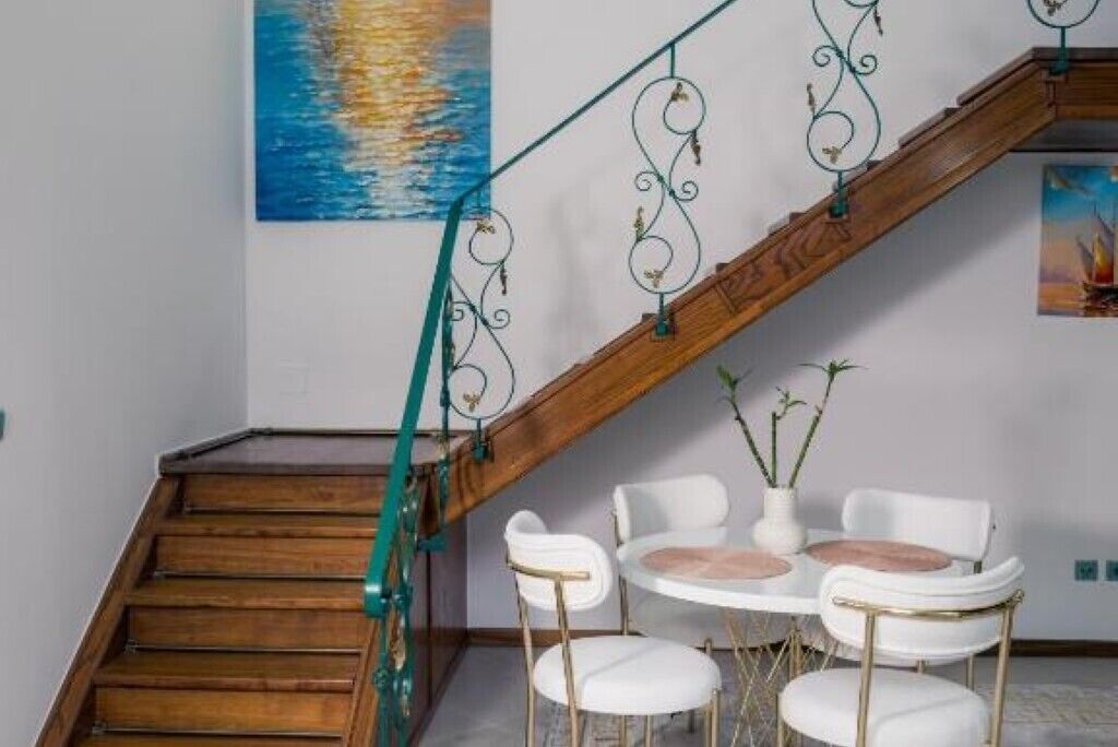 A staircase with a wooden handrail and green metal balusters, leading to a white round table with four chairs.