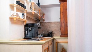 A compact kitchen with a coffee machine, shelves with kitchenware, and a wooden cabinet. - Apartament 3 (Timișoara)