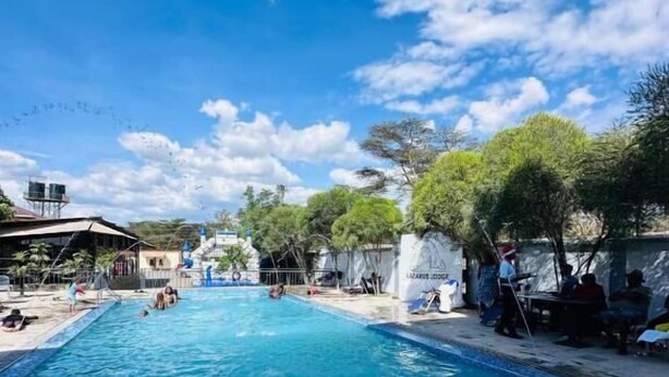 Une piscine à l’eau d’un bleu cristallin, entourée d’arbres et d’un bâtiment sur lequel on peut lire l’inscription « LAZARO’S LODGE ».